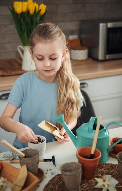 Little girl sitting at the table at home sowing seeds into flower pots