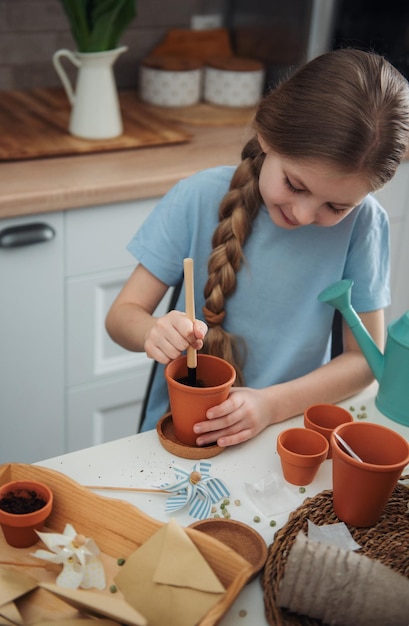 Little girl sitting at the table at home sowing seeds into flower pots