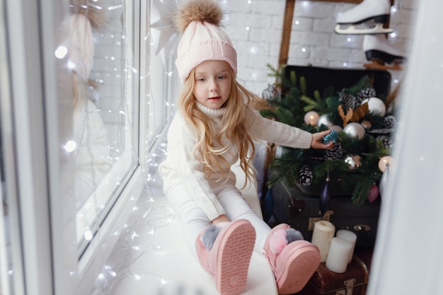 Little girl sitting on a window sill in Christmas morning.