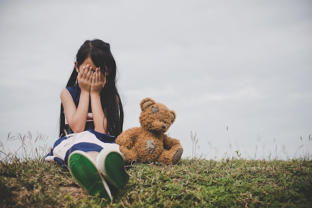 Little girl sitting with her bear upset at meadows field