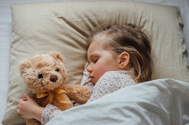 Little girl sleeping in bed embracing soft toy at home, top view