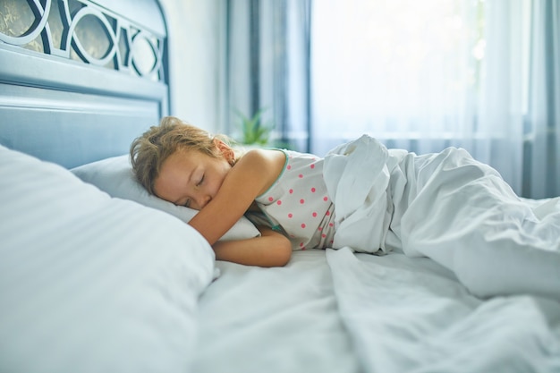 Little girl sleeping on a big and cozy bed white linen in the afternoon at home