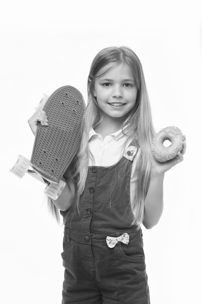 Little girl smile with skateboard and donut isolated on white Child skater with doughnut and longboard Skateboard kid with junk food Sport and energy Food for snack and dessert dieting concept