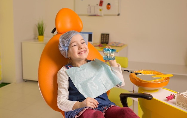 A little girl smiles and holds a model of a jaw in her hands while sitting on a chair in a dental clinic Dental care oral hygiene