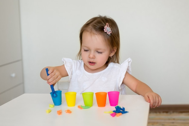 A little girl sorts the animal figures by color, throwing them into the appropriate cup.