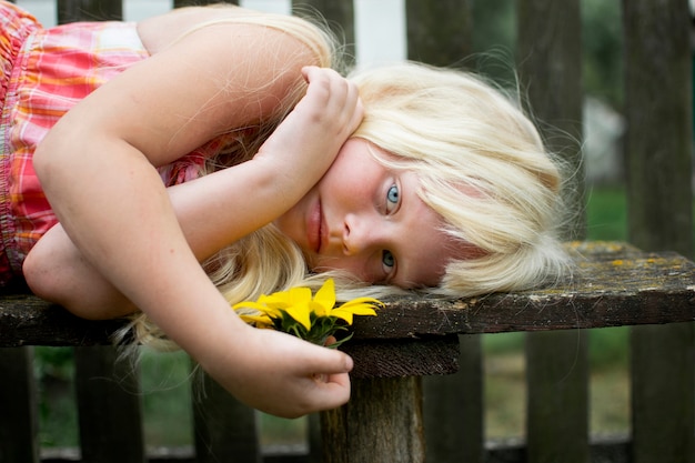 A little girl spends the weekend in the village. Summer, greenery, blue sky. Wooden fence