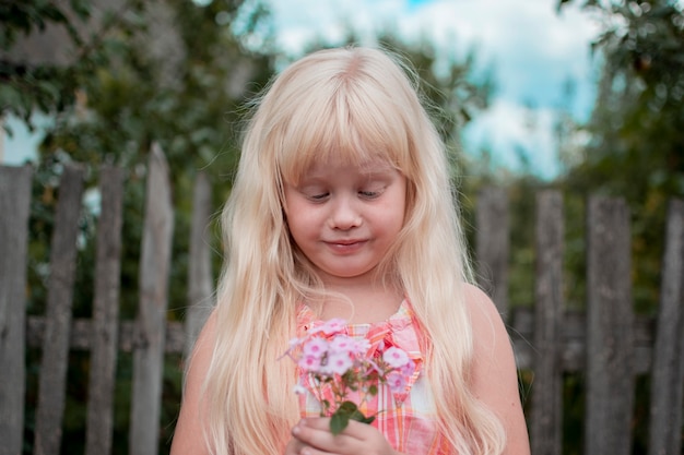 A little girl spends the weekend in the village Summer greenery blue sky Wooden fence