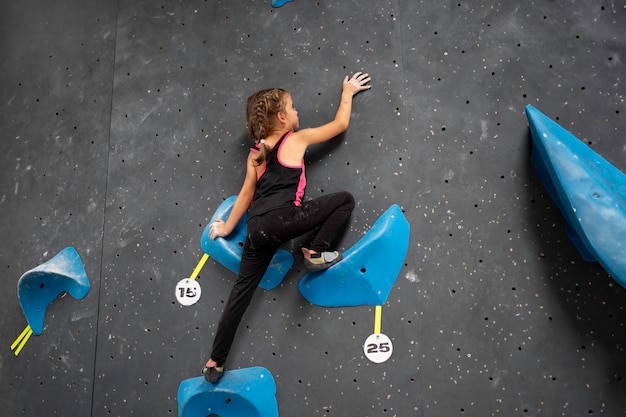 Little girl in sportswear is climbing wall entertainment center