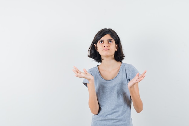 Little girl spreading open palms in t-shirt and looking confused. front view.