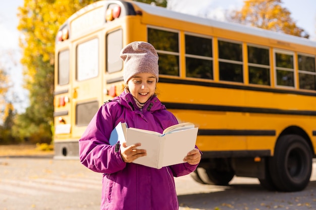 Little girl standing by a big school bus with her books.