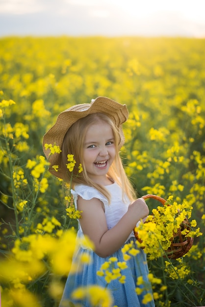 Little girl standing in a field, basket of flowers, laughing, rapeseed flower field