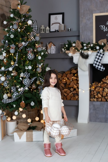 Little girl standing with artificial snowballs in the living room by Christmas tree