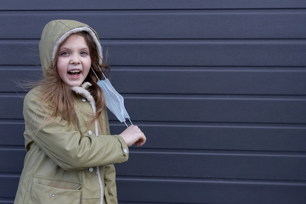 A little girl on the street joyfully removes the medical mask