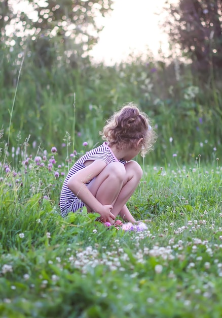 Photo little girl in striped dress of chool age collects ripe strawberry in the kitchengarden happy childhood in countryside