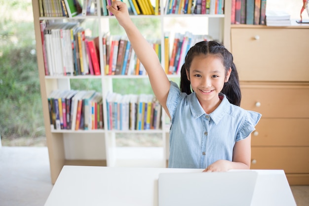 Little girl student with laptop at desk in library and fighto acting