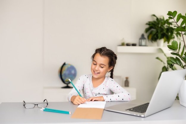 Little girl studying online using her laptop at home