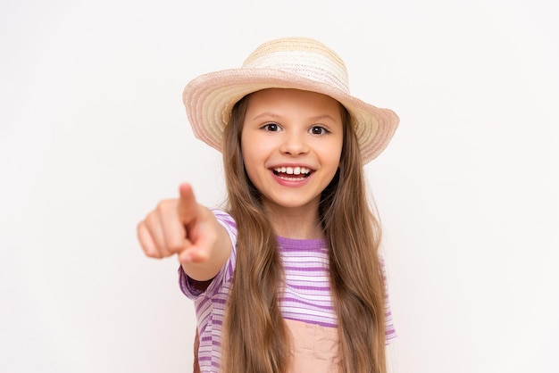 A little girl in a summer sundress and a straw hat points at you with her index finger The concept of summer holidays for children