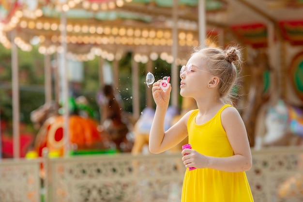 A little girl in sunglasses blows soap bubbles in the park in the summer