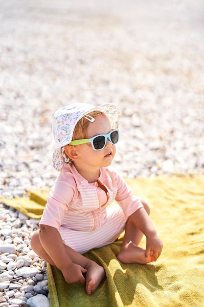 Photo little girl in sunglasses sits on the beach