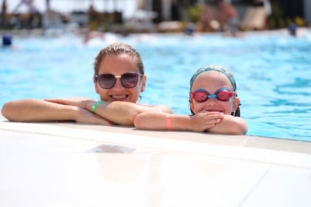 Little girl in swimming goggles and mother lying on side of pool