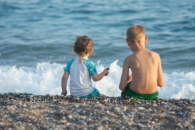 A little girl in a swimsuite plays with her brother in the sand on the sea beach