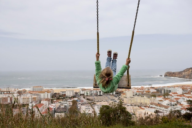 Little girl swinging against the scene of nazare coast in portugal