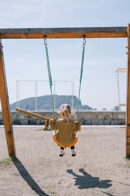 Photo little girl swings on a rope swing on a playground by the sea back view