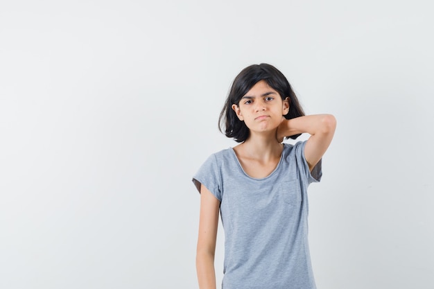 Little girl in t-shirt holding hand on neck and looking pensive , front view.