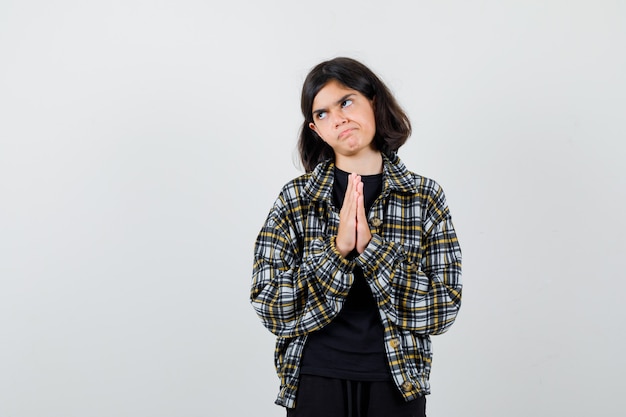 Little girl in t-shirt, jacket showing clasped hands in pleading gesture and looking hopeful , front view.