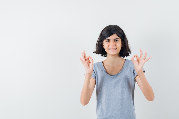 Little girl in t-shirt showing ok gesture and looking cheery , front view.