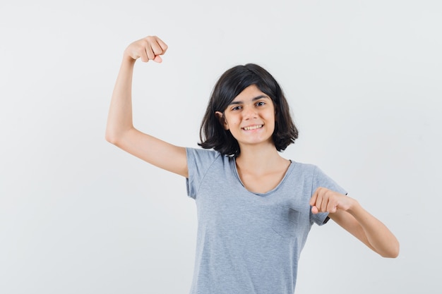 Little girl in t-shirt showing winner gesture and looking lucky , front view.