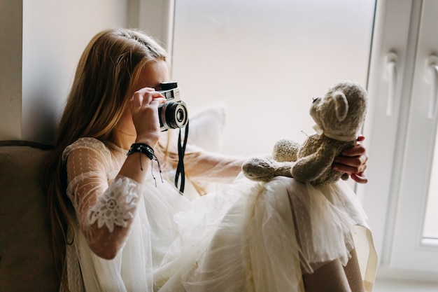 Little girl taking photo of plush bear with an old camera