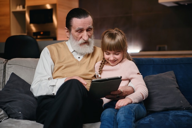 Little girl teach grandpa to use modern smart devices. Communication of young and senior generation. Enjoy leisure time with family.