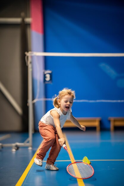 Little girl three years old playing badminton in sport wear on indoor court