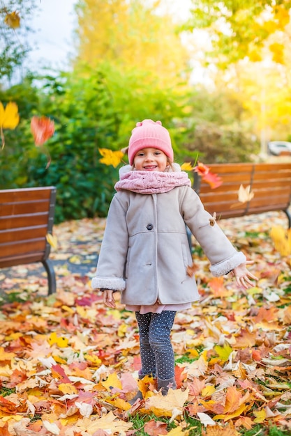 Little girl throwing leaves in the autumn park