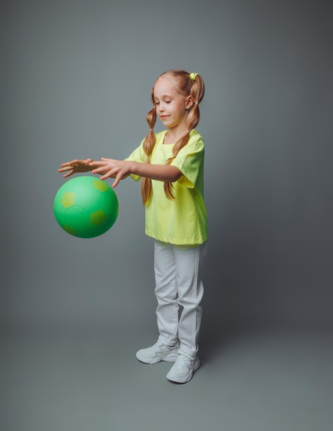 A little girl throws a ball up isolated on a gray background a little athletechildren's sports