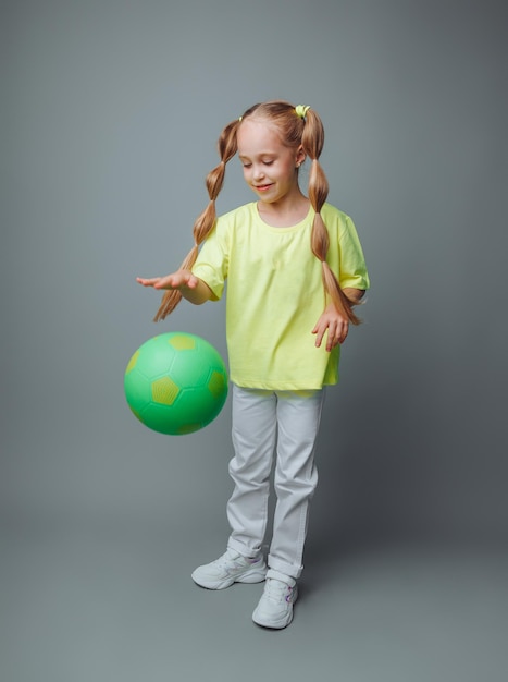 A little girl throws a ball up isolated on a gray background a little athletechildren's sports