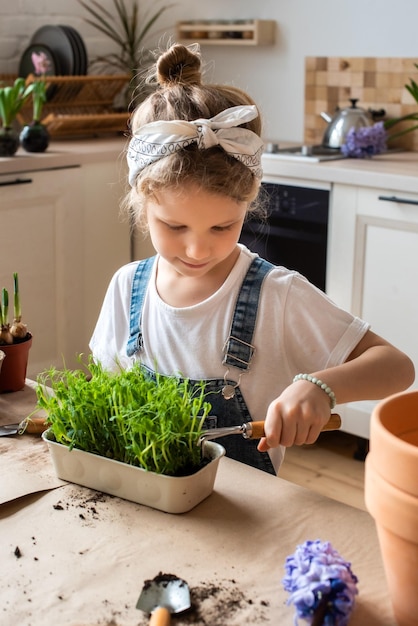 Little girl transplants flowers and houseplants a child in a bandana plants bulbs and microgreens