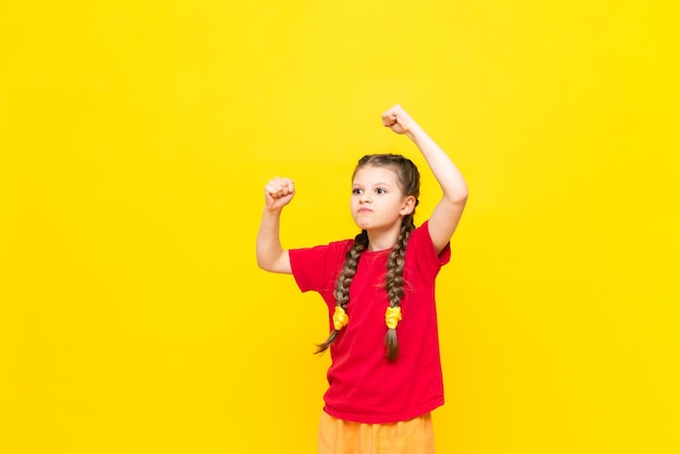 The little girl viciously shows her fists with her hands up A disgruntled child is protesting against a yellow isolated background