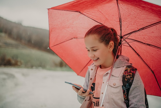 Little girl waiting for bus on rain day and using phone