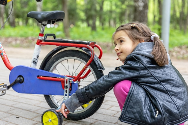 Photo little girl on a walk in the park with her bike.