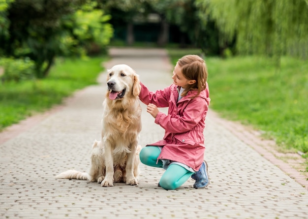 Little girl walking with golden retriever in green park