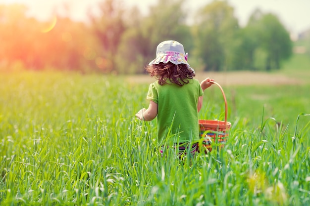 Little girl walking with picnic basket on the green field back to camera