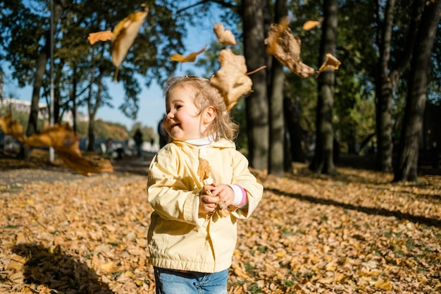 Little girl walks in the park in autumn and throws leaves.