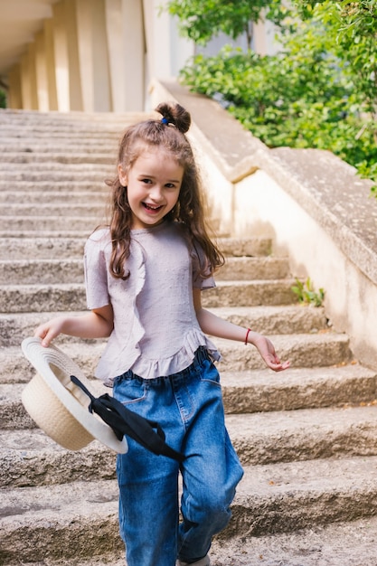 A little girl walks up the steps in the park and holds a hat in her hands.