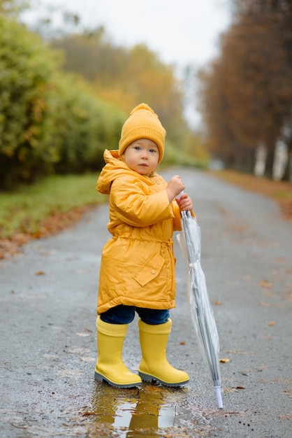 A little girl walks with an umbrella in yellow rubber boots and a waterproof raincoat Autumn Walk