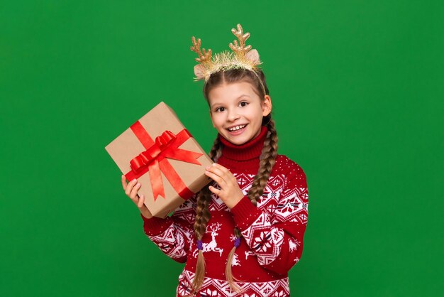 A little girl in a warm Christmas sweater holds a gift and smiles the concept of the new year isolated background