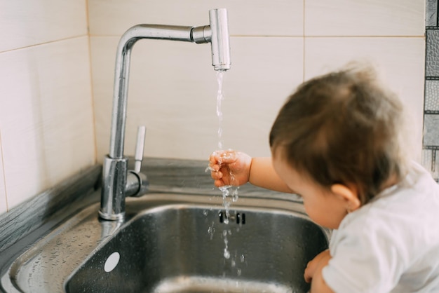 Little girl washes her hands in the kitchen by herself