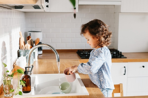 Little girl washing dishes in the kitchen at home