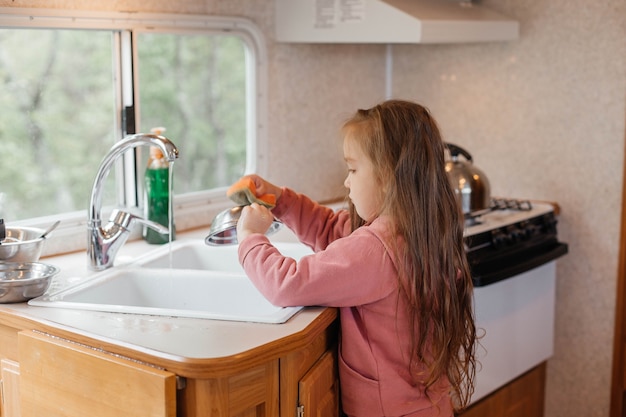 Little girl washing dishes in the kitchen of a travel trailer